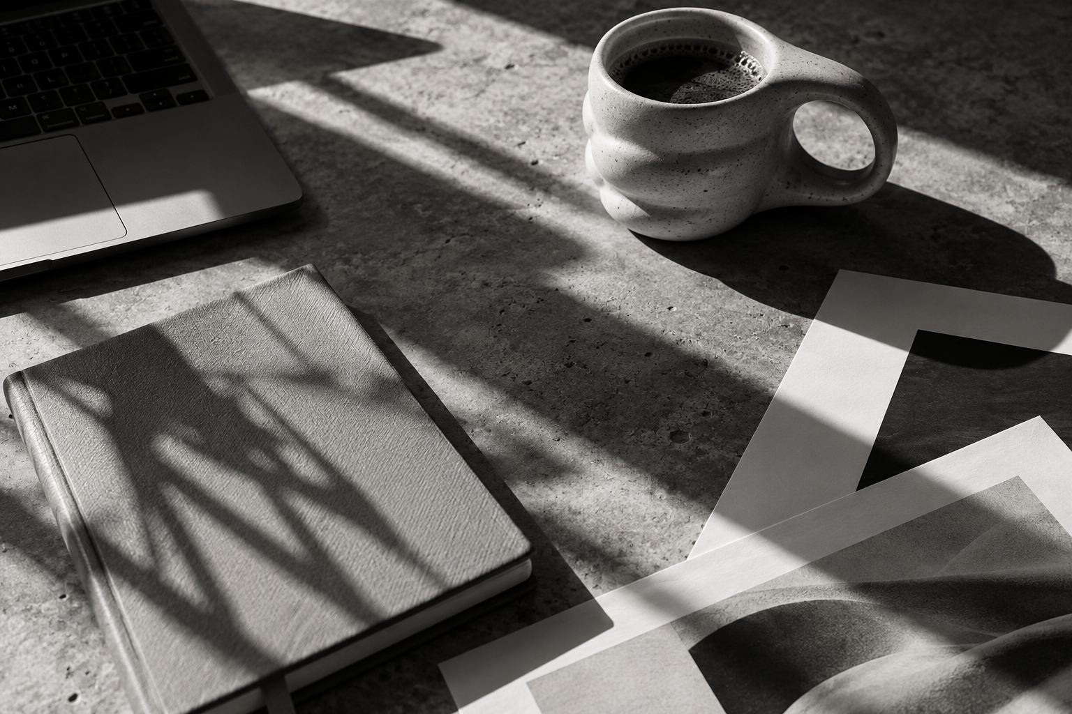 A sunlit creative workspace with a notebook, laptop and printed layouts